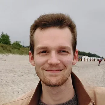 Dennis lächelt in die Kamera, im Hintergrund ein Strand mit Strandkörben.